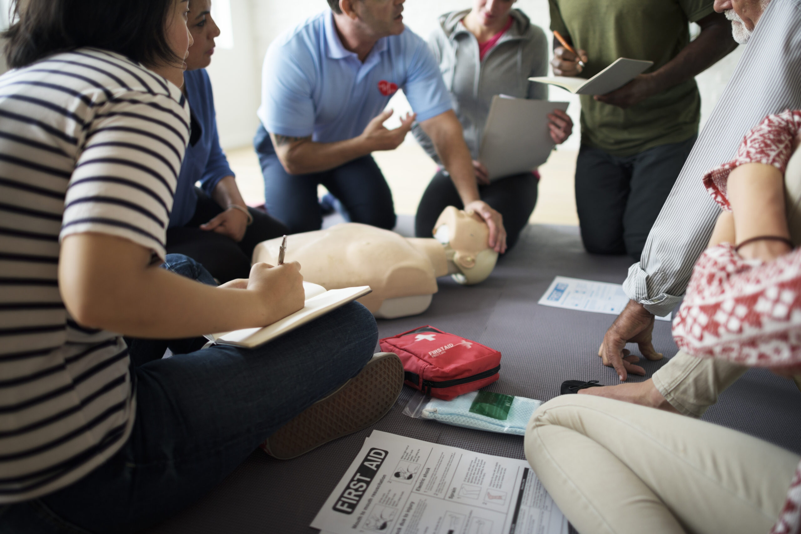 Grupo de personas en curso de primeros auxilios practicando técnicas de emergencia con muñeco de RCP