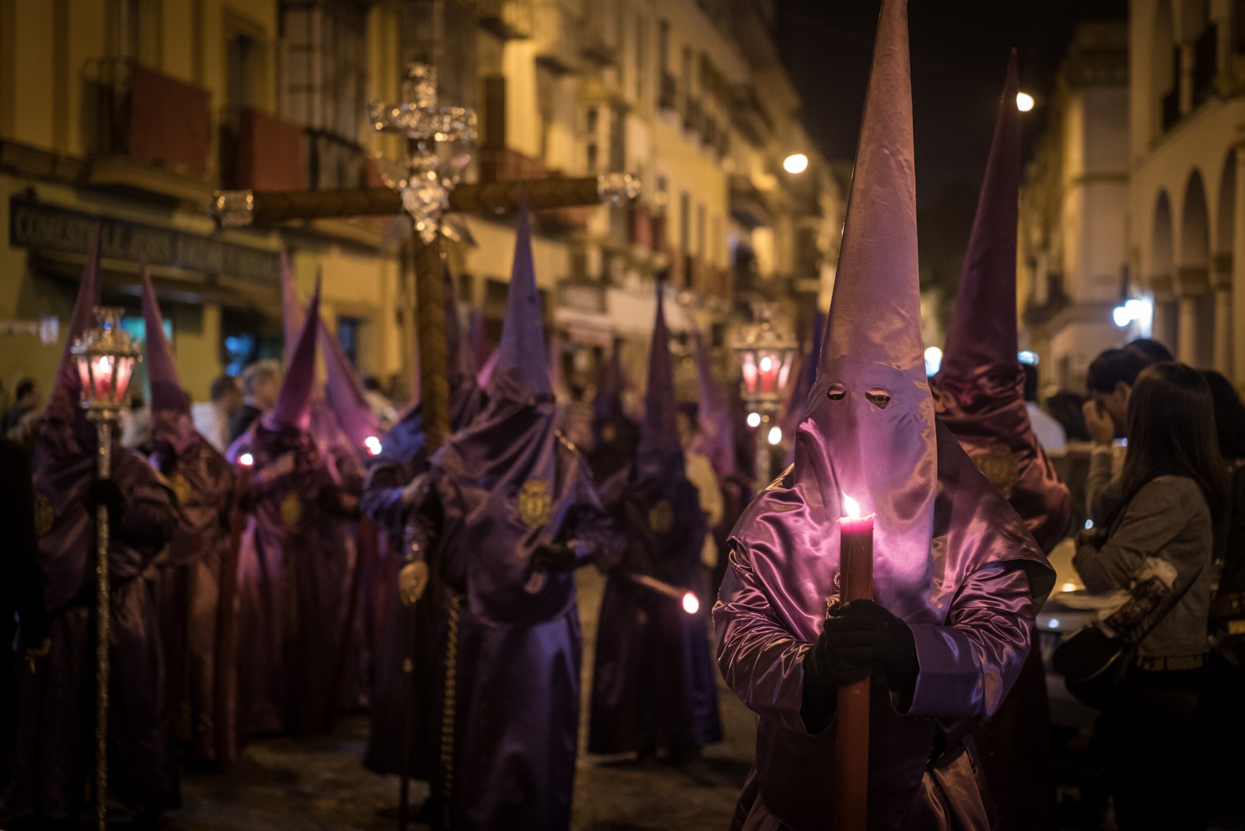 Nazarenos en procesión de Semana Santa con túnicas y velas en una calle nocturna