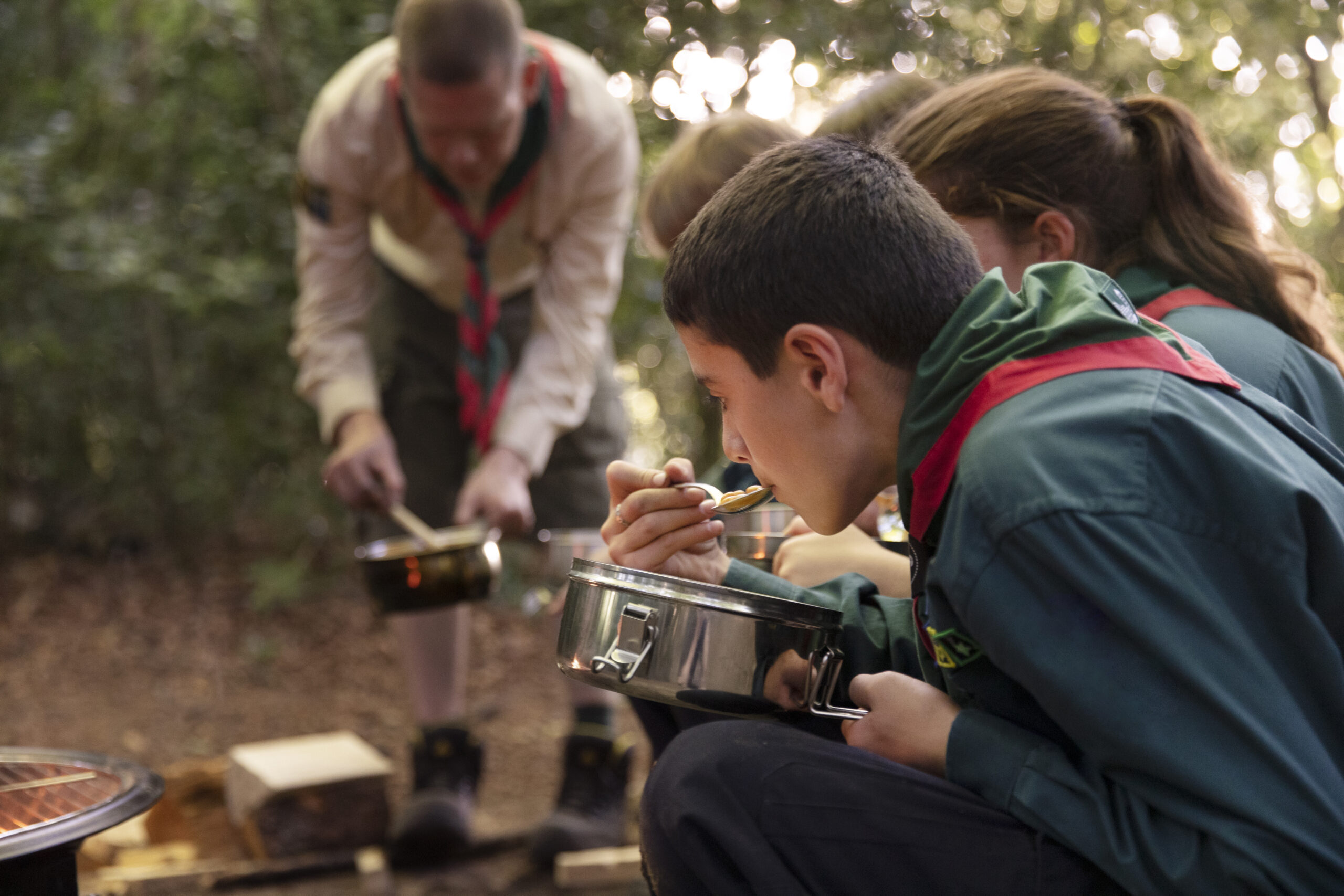 Niños comiendo al aire libre en un campamento guiados por un monitor