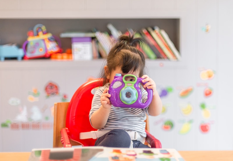 Niña pequeña jugando con una cámara de juguete en un aula infantil.