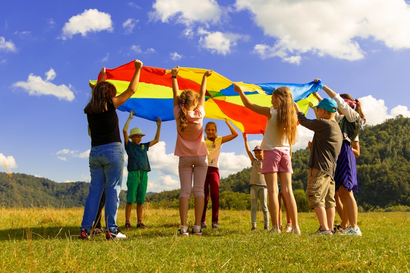 Niños jugando con un paracaídas de colores en una actividad al aire libre durante un campamento de verano.